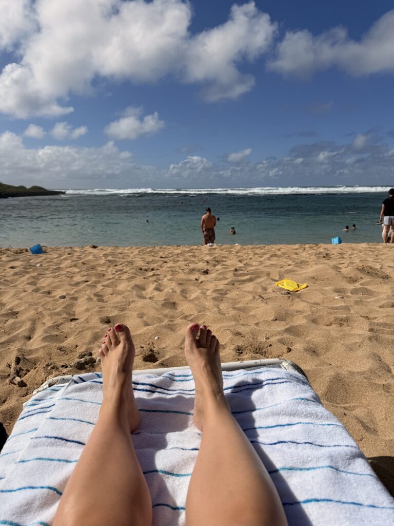 Hawaiian beach with white sand and crystal blue water with a person laying out and enjoying the sunshine