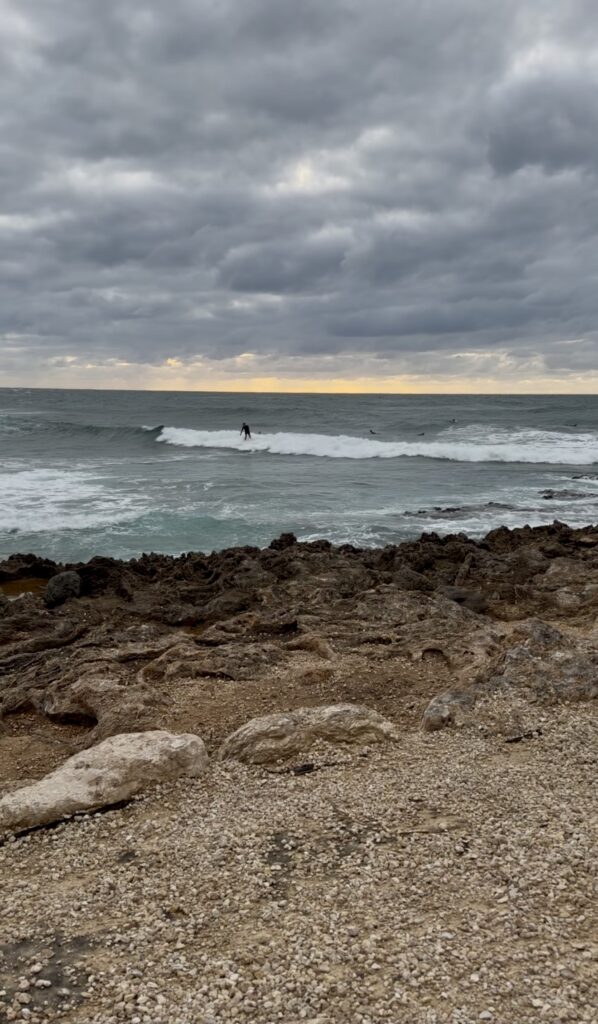 surfer riding a wave under cloud coverage in Hawaii's North Shore at husband and wife cozy on the balcony at The Ritz-Carlton Oahu, Turtle Bay